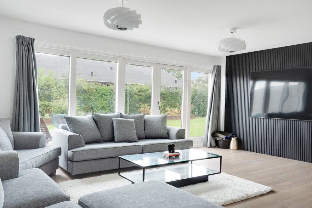 Stue med grå sofaer, store vinduer og sort rillevæg med tv
